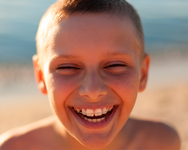 Imagem ilustrativa de uma pessoa sorrindo com aparelhos ortodônticos, em um cenário de verão.
