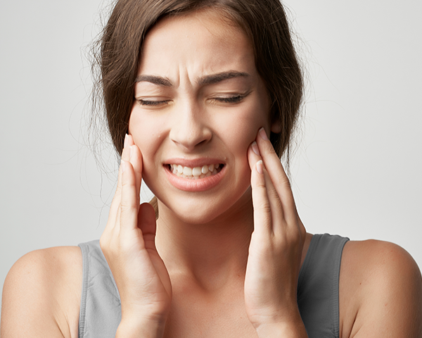 Pessoa com mão na mandíbula expressando dor, representando os sintomas do bruxismo.