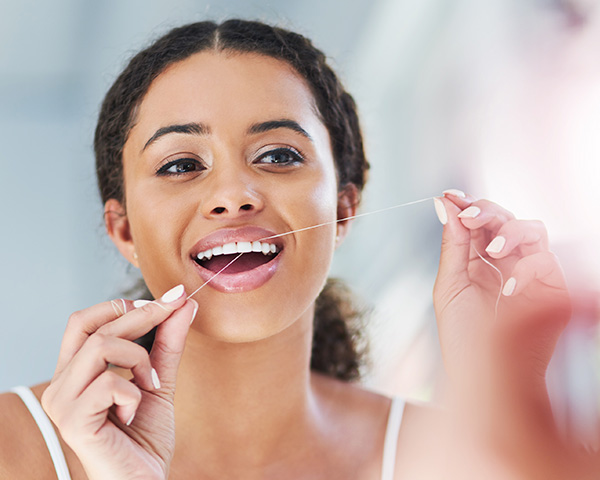Pessoa cuidando da saúde bucal escovando os dentes com escova e fio dental 